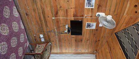 A wooden-paneled room with a bed, a chair, a desk, and a wall-mounted TV.