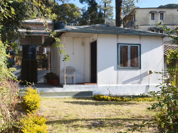 A small, single-story house with a white exterior, a green-framed window, and a small porch with a white chair. - Tip N Top (Lansdowne)