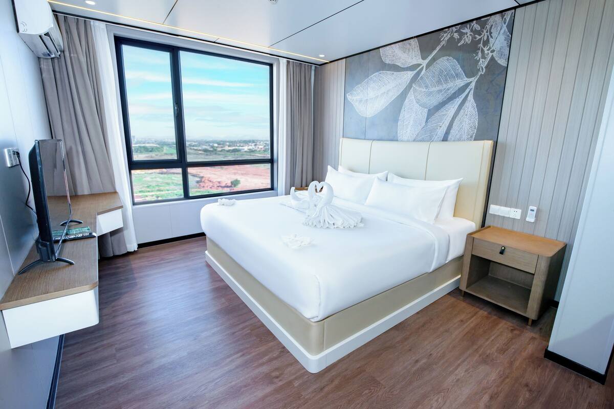 Een moderne hotelkamer met een groot bed, een televisie op een standaard, een nachtkastje en een raam met uitzicht op de stad.