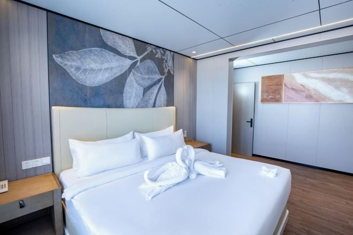 Quarto de hotel moderno com uma cama grande, cabeceira, mesa de cabeceira e parede com padrão de folhas.