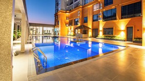 Et moderne hotel med swimmingpool, udendørs siddepladser og en godt oplyst facade.