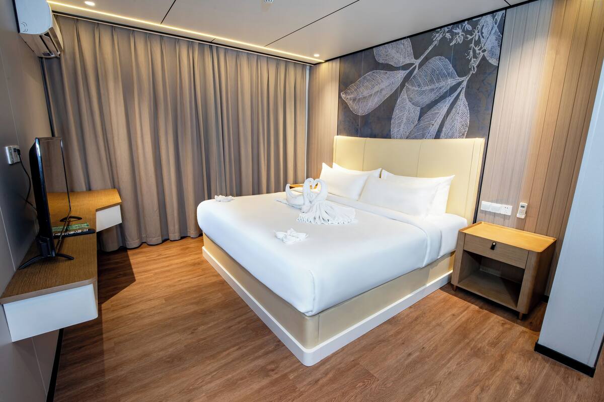 Een moderne hotelkamer met een groot bed, nachtkastje, televisie en een wandairconditioner.