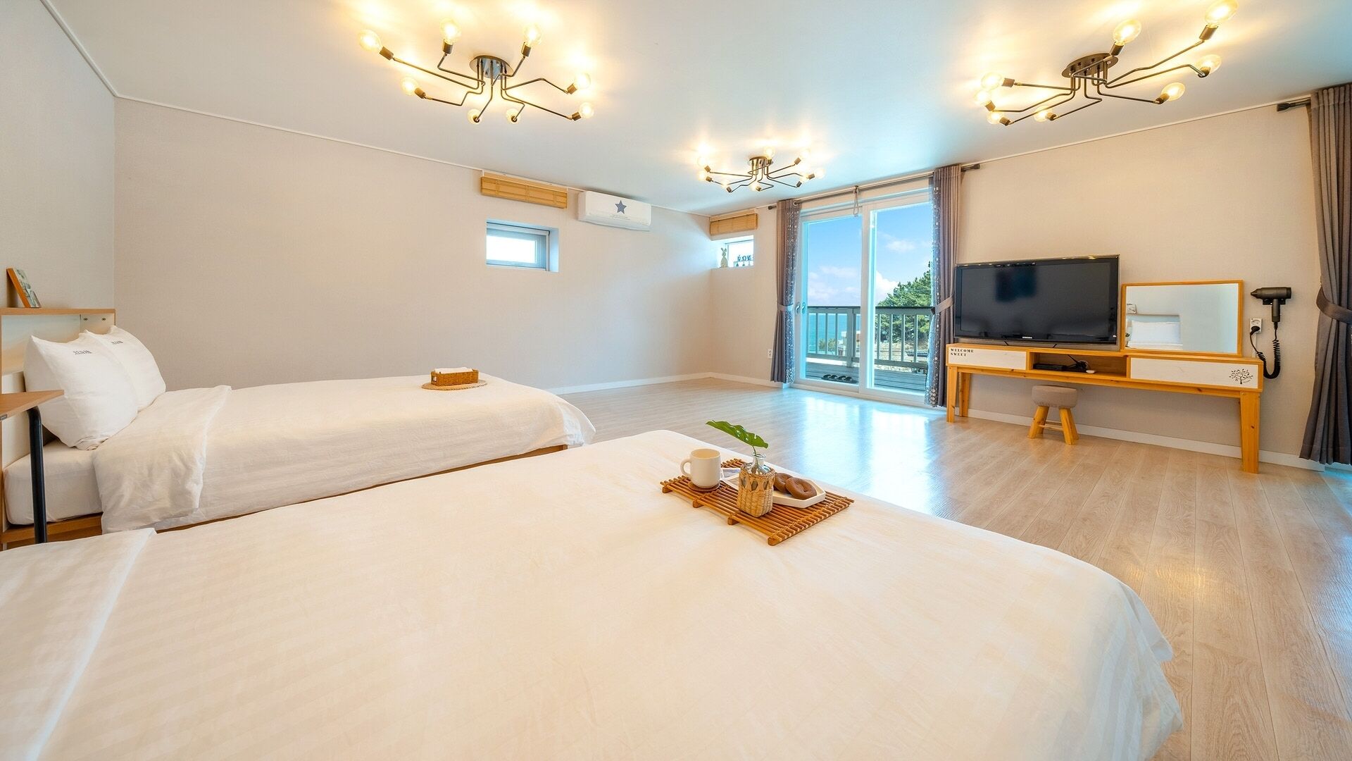A hotel room with two beds, a TV, a desk, and a balcony with a view.