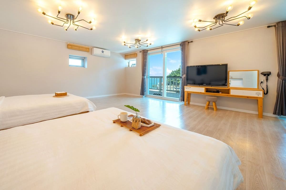 A hotel room with two beds, a TV, a desk, and a balcony with a view.