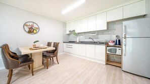Una cocina moderna con armarios blancos, un refrigerador de acero inoxidable y un microondas. Hay una mesa de comedor con sillas y un elemento decorativo en la pared.