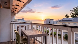 Een balkon met uitzicht op de ondergaande zon boven de oceaan, een tafel en twee stoelen.