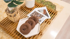Un plato con dos galletas, una taza blanca, una cesta de mimbre y una revista sobre una estera de bambú.
