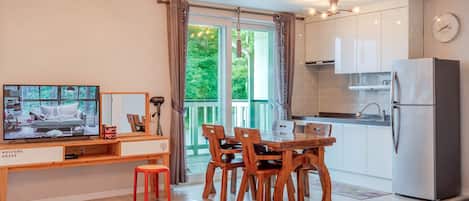 A modern kitchen with a dining area, a TV, and a view of greenery outside.