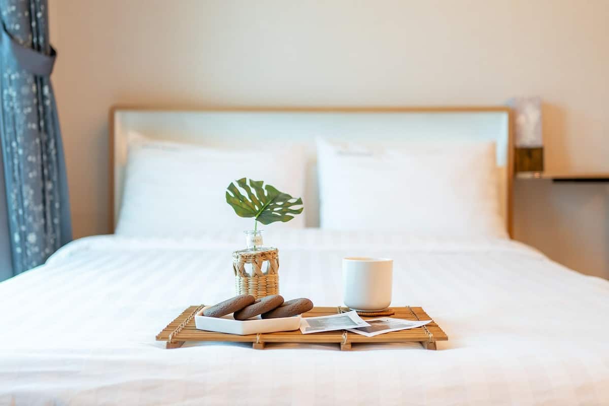 Una cama bien hecha con una bandeja de galletas, una taza y una planta sobre una bandeja de madera.