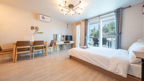 Habitación de hotel con una cama grande, un escritorio con silla, un televisor y una ventana con vistas a árboles.