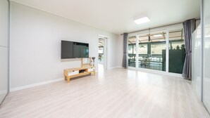 Amplia sala de estar con un televisor de pantalla plana montado en la pared, un mueble de entretenimiento de madera y un amplio ventanal corredera que da a un patio exterior.
