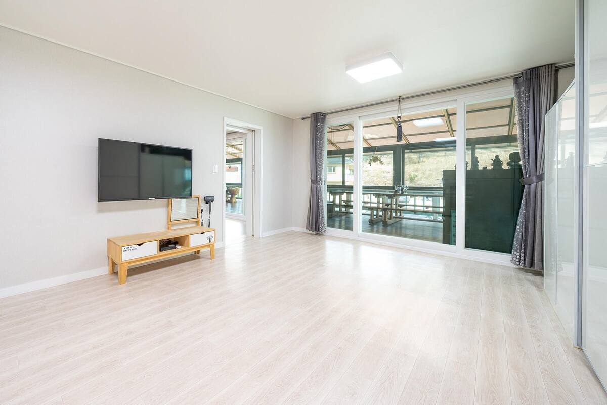 Amplia sala de estar con un televisor de pantalla plana montado en la pared, un mueble de entretenimiento de madera y un amplio ventanal corredera que da a un patio exterior.