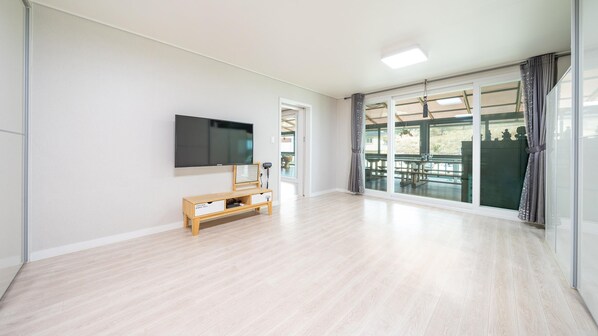 Amplia sala de estar con un televisor de pantalla plana montado en la pared, un mueble de entretenimiento de madera y un amplio ventanal corredera que da a un patio exterior.