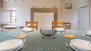 Een eetkamer met een tafel voor vier personen, voorzien van een tafelkleed met een patroon, houten stoelen en een decoratieve schaal in het midden.