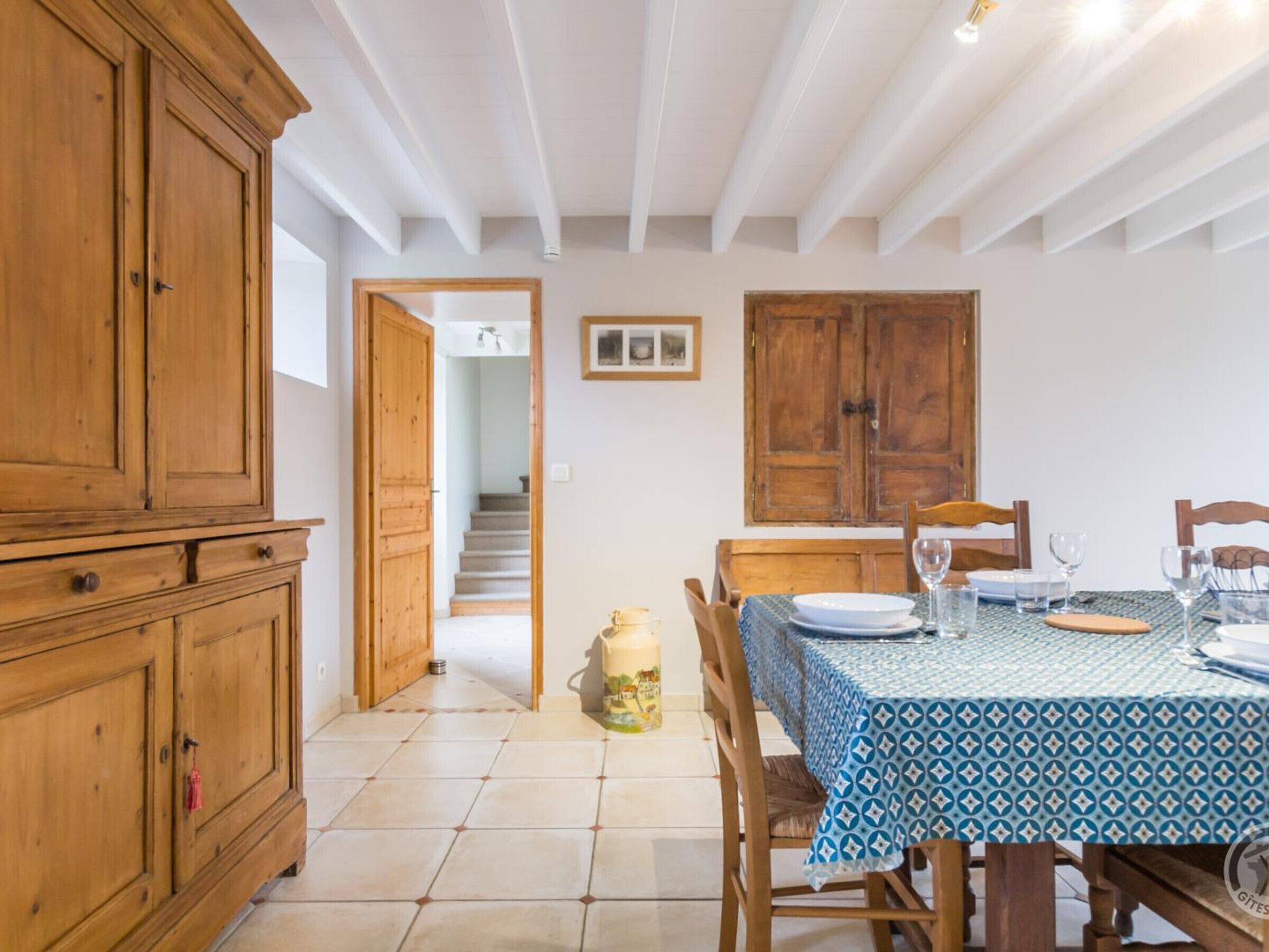 A dining area with a table set for four, wooden cabinets, a staircase, and a door leading to another room.