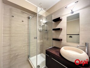 Une salle de bain moderne dotée d’une douche à parois de verre, d’un grand lavabo et d’étagères intégrées.