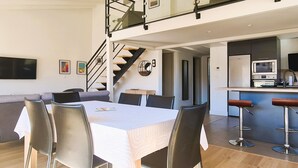 Une cuisine moderne équipée d’un four à micro-ondes, d’un évier et d’un coin bar. On y trouve également un coin repas avec une table et des chaises. Un escalier relie les deux niveaux.