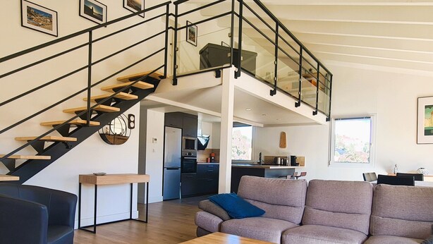 Un espace de vie moderne comprenant un escalier, un canapé, une table basse et un coin cuisine.