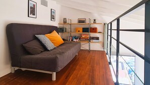 Un salon moderne avec un canapé marron foncé, un plancher en bois et une porte en verre donnant sur un balcon.