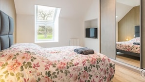 A bedroom with a bed, a television, a large mirror, and a window with a view of trees.