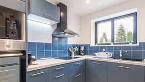 A modern kitchen with blue cabinets, a built-in oven, a coffee maker, and a window with a view of trees.