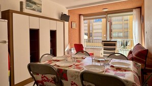 A dining area with a table set for four, chairs with floral patterns, a kitchen area with cabinets, and a balcony with a railing. - 2-room apartment near beach with pool (Argelès-sur-Mer)