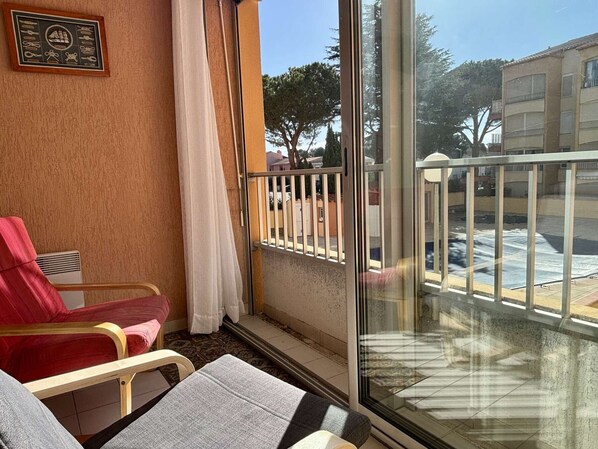 Un balcon avec une porte vitrée, une chaise rouge, un canapé gris et un tableau encadré au mur.
