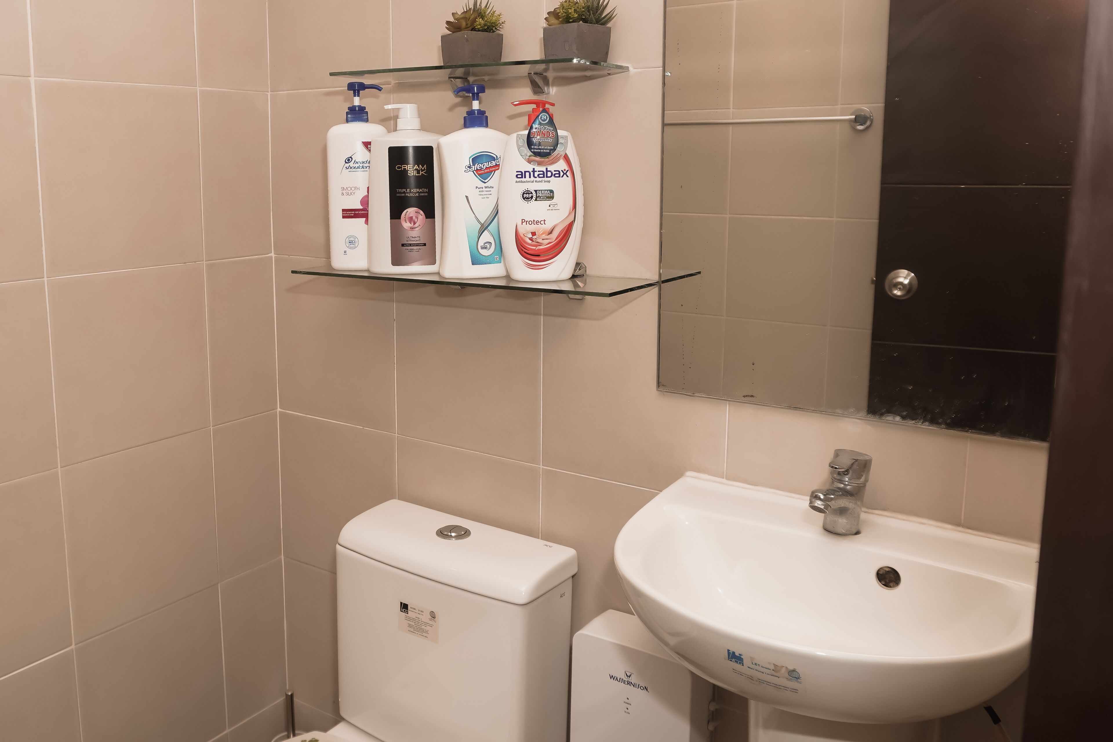 A bathroom with a toilet, a sink, and a shelf with three bottles of toiletries.