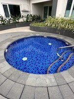 Una piscina circular con mosaicos azules, rodeada de losetas de piedra gris y una barandilla de metal.
