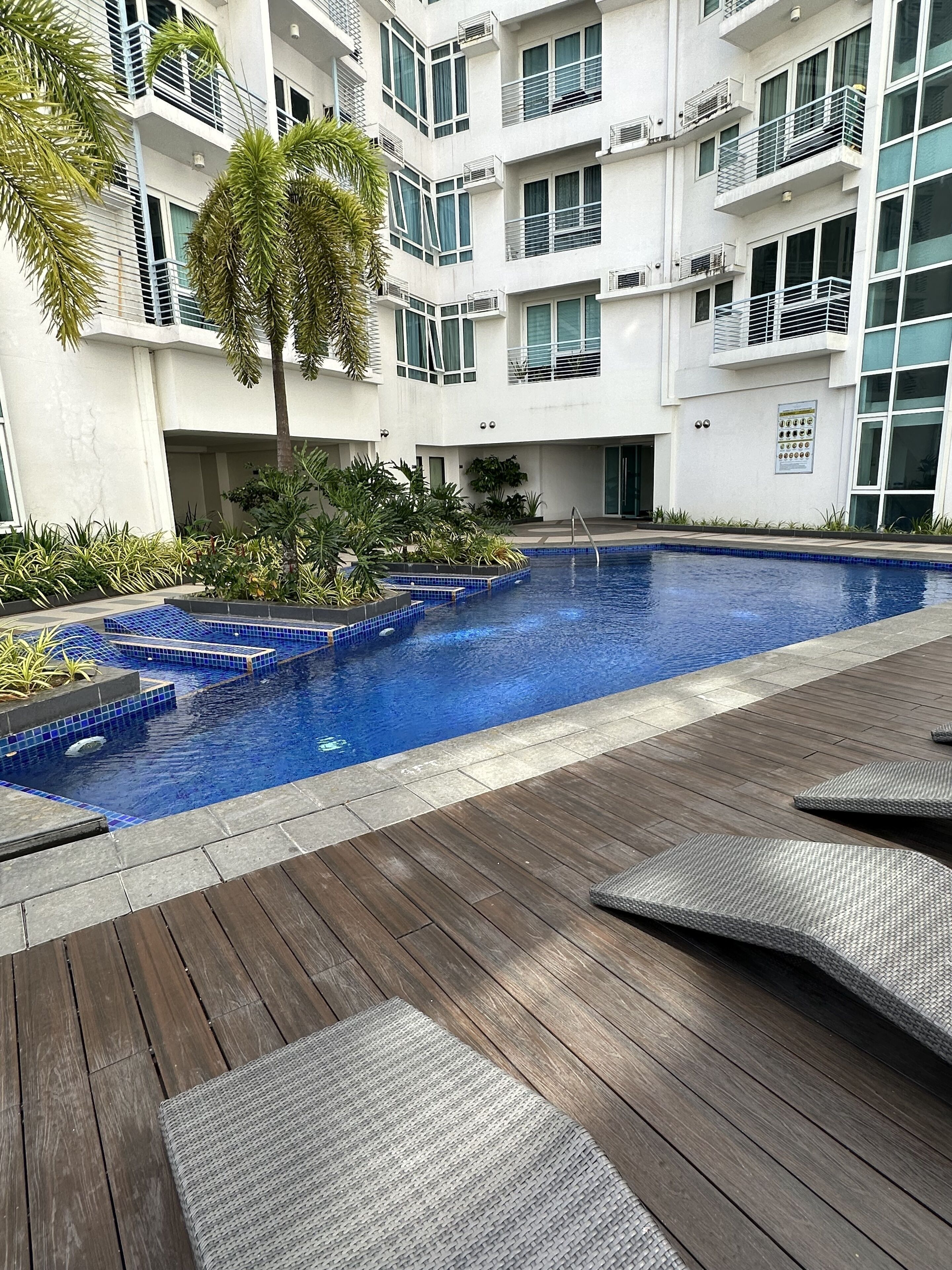 Un edificio moderno con piscina, terraza de madera y asientos al aire libre.