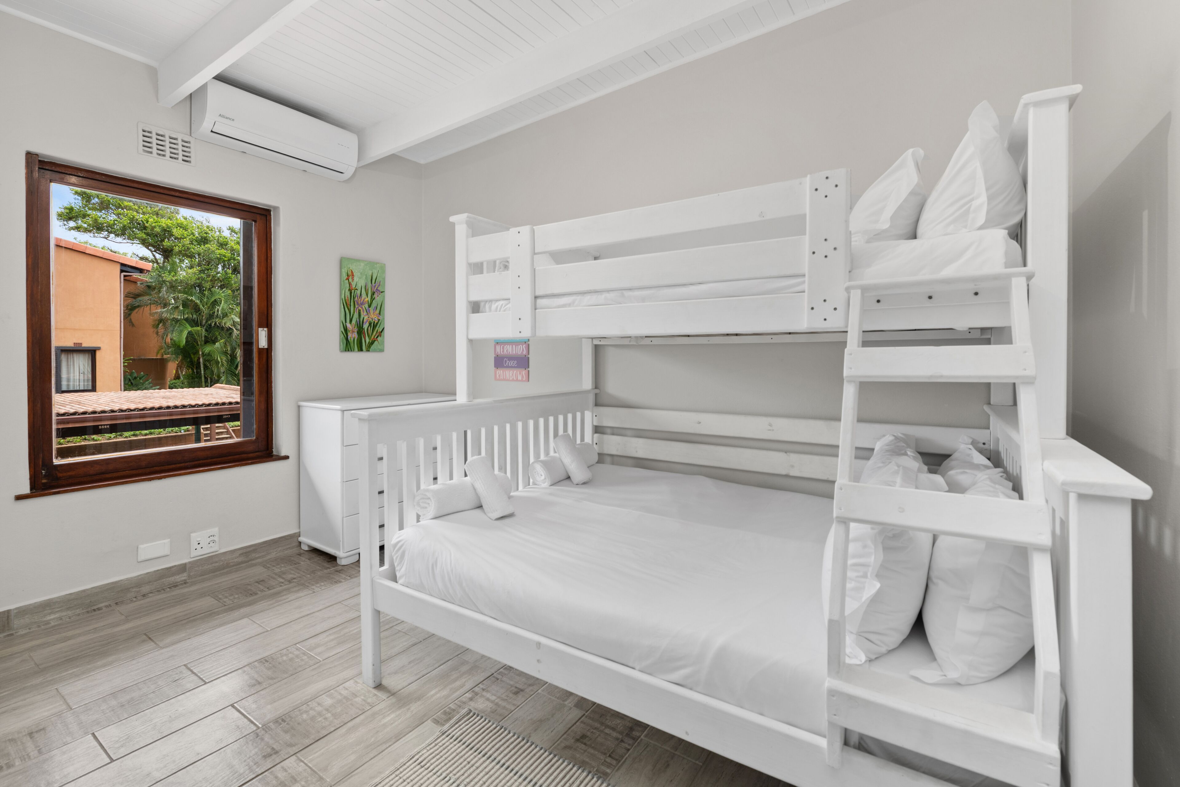 A bunk bed room with a window, white walls, and a wooden floor.