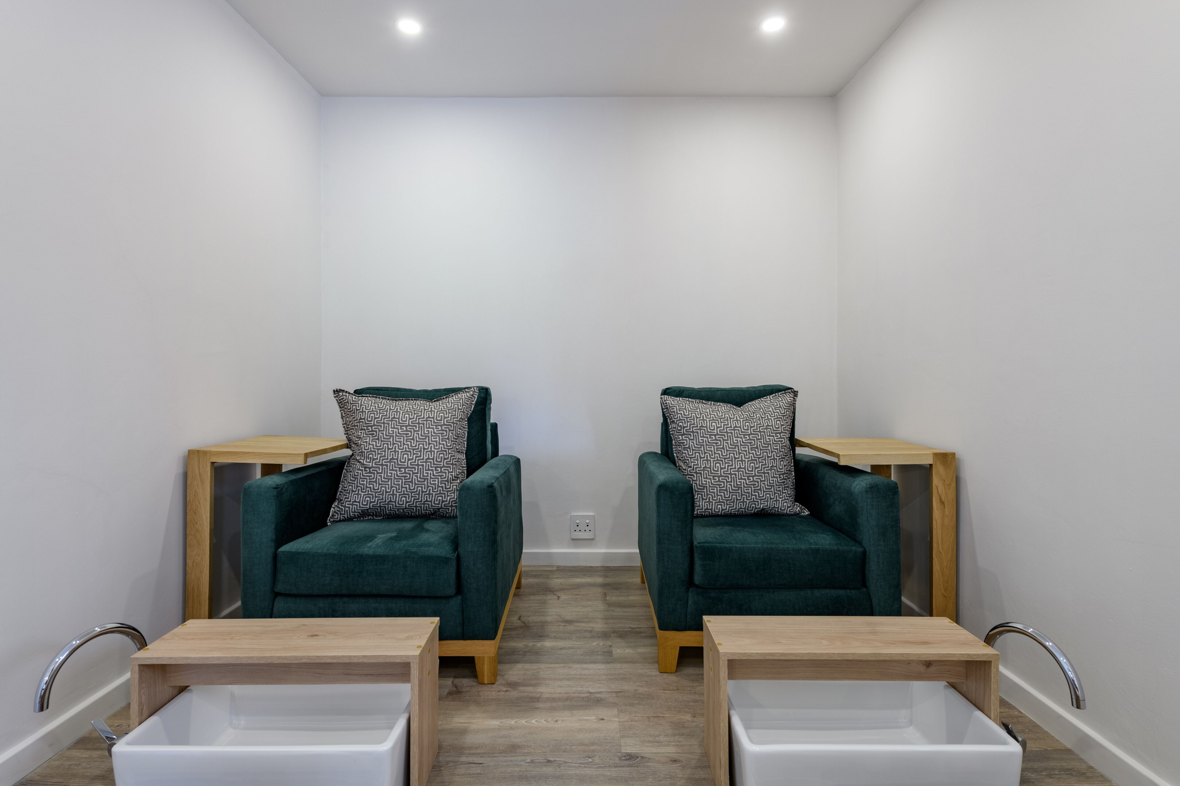 A room with two green armchairs, each with a patterned pillow, and a white sink between them.