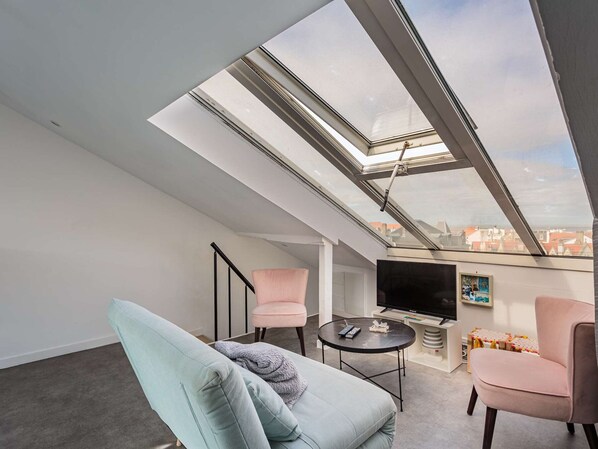 A modern living room with a skylight, a flat-screen TV, and two chairs.