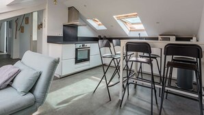 Une cuisine moderne dotée de fenêtres de toit, un coin repas avec des tabourets de bar et un canapé de couleur claire.