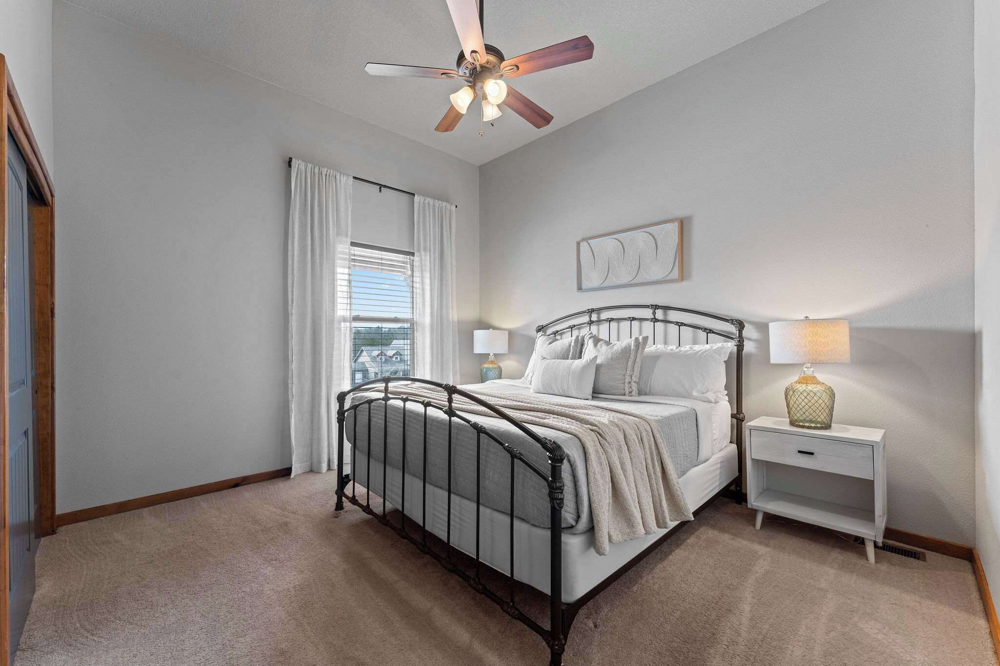 A bedroom with a bed, a nightstand, a lamp, a ceiling fan, and a window with curtains.