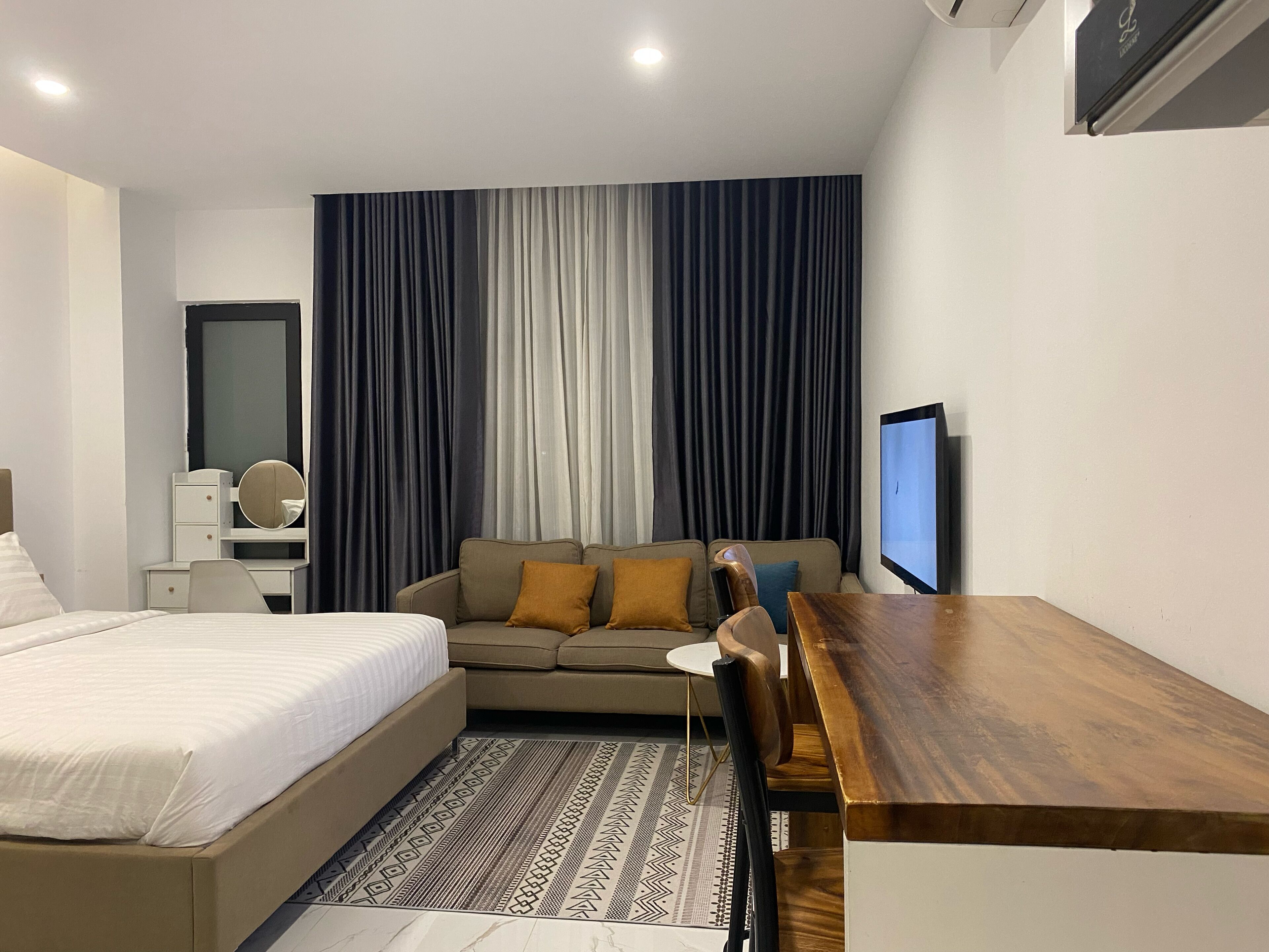 A modern hotel room with a bed, a sofa, a desk, and a TV.