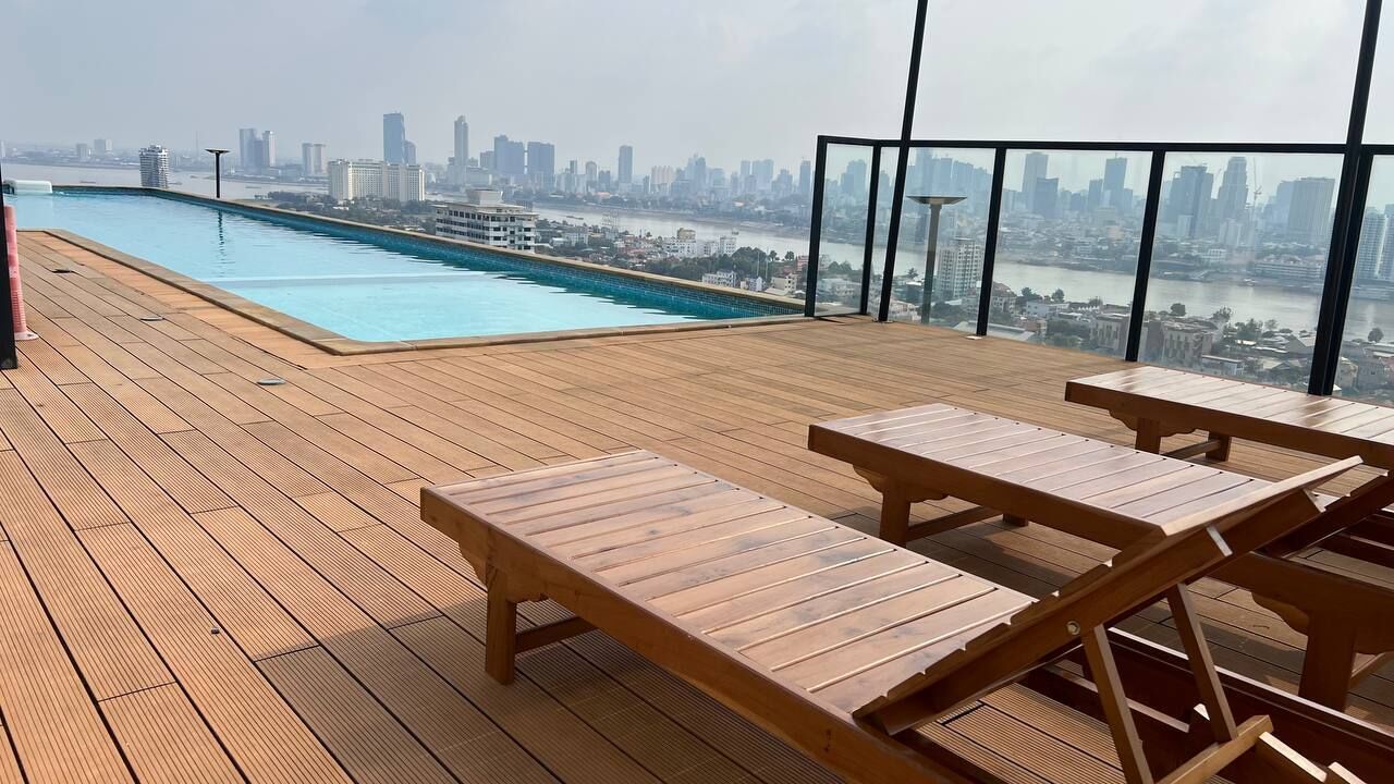Une piscine sur le toit, dotée de chaises longues en bois et offrant une vue sur la ville.