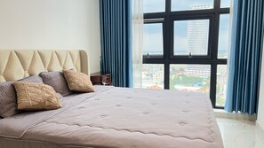 Un dormitorio con una cama grande, un cabecero capitonado y vistas a un paisaje urbano a través de una ventana.