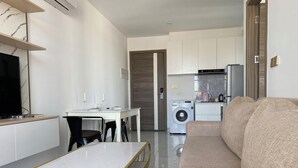 Een moderne woonkamer met een bank, een eettafel met stoelen, een televisie en een wasmachine op de achtergrond.
