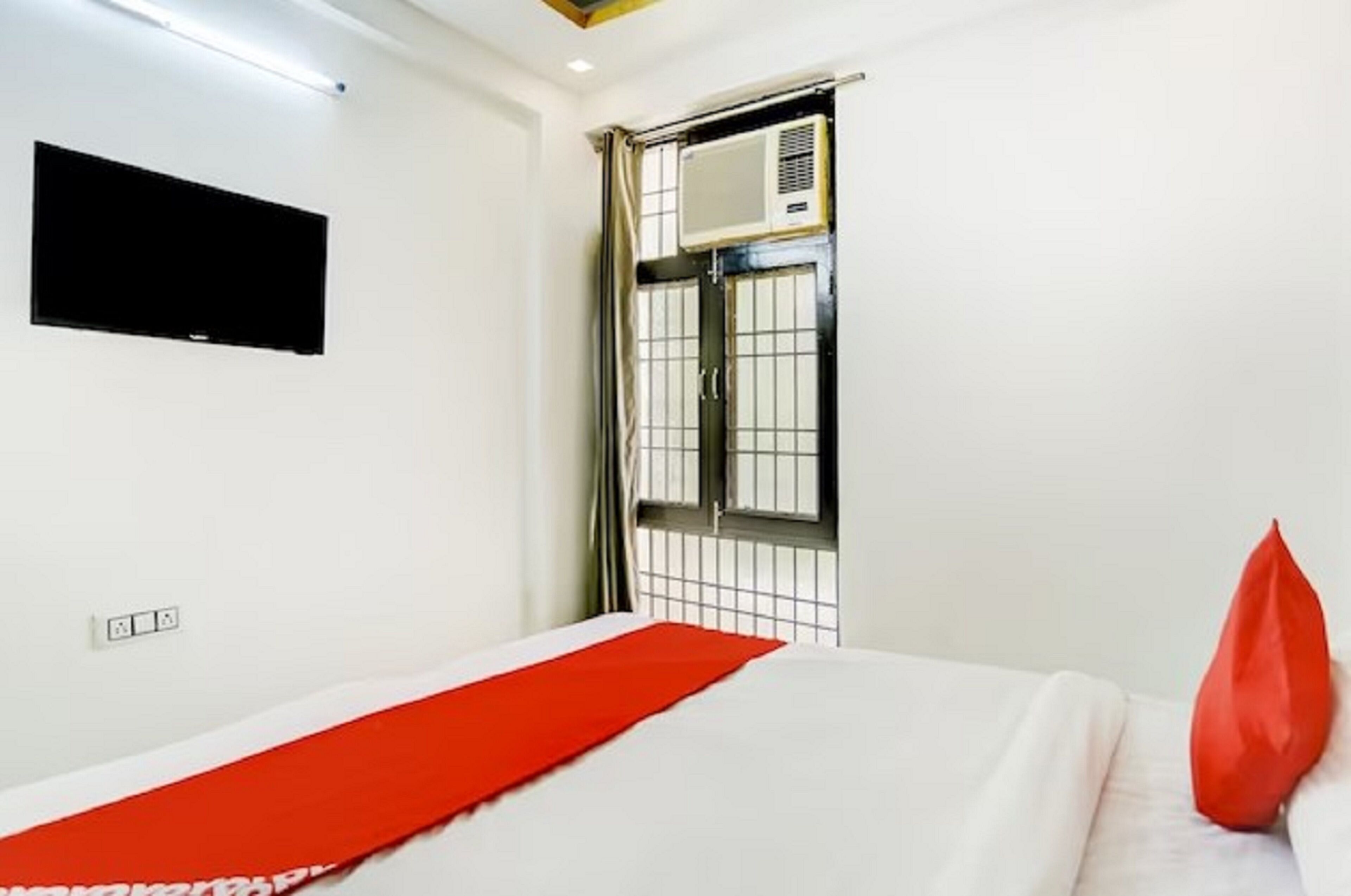 Habitación de hotel con cama, televisor de pantalla plana en la pared, aire acondicionado y ventana con celosía de metal.