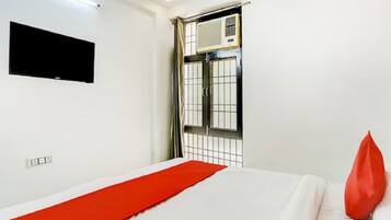 Habitación de hotel con cama, televisor de pantalla plana en la pared, aire acondicionado y ventana con celosía de metal.