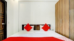 Un dormitorio con una cama, dos almohadas rojas, un armario de madera y una pared blanca.