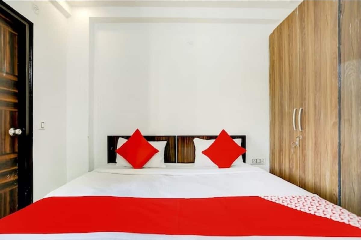 A bedroom with a bed, two red pillows, a wooden wardrobe, and a white wall.