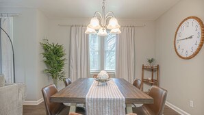 Una sala da pranzo con un tavolo in legno, poltrone in pelle, un lampadario, una sveglia e una pianta in vaso.