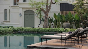 Área de piscina com espreguiçadeiras e uma árvore.