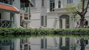 Um edifício refletido em águas calmas, com uma árvore e uma sebe bem cuidada.