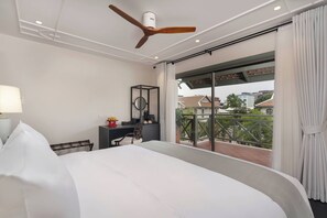 Une chambre d’hôtel dotée d’un grand lit, d’un bureau avec une chaise, d’un ventilateur de plafond et offrant une vue sur la ville grâce à une porte-fenêtre coulissante.