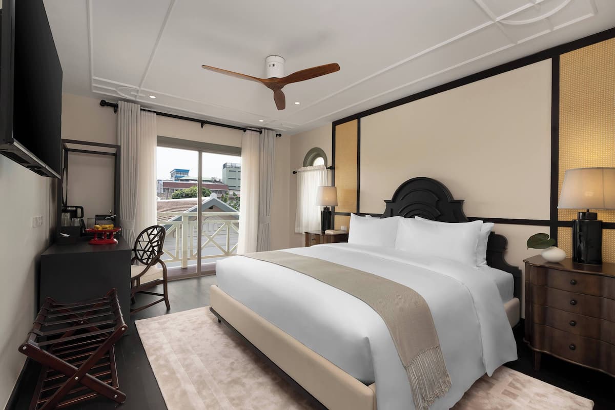 Hotelkamer met een groot bed, een bureau met stoel, een plafondventilator en uitzicht op buiten.