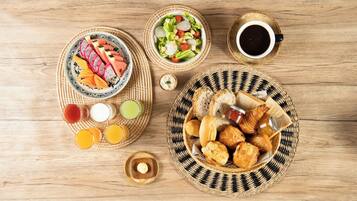 A breakfast spread on a wooden table with various dishes, including fruits, pastries, and beverages.