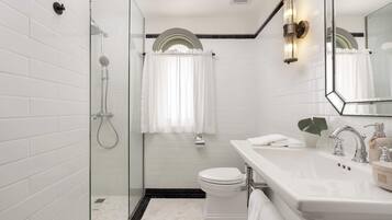 Et moderne badeværelse med bruseniche i glas, et hvidt toilet og en vask med spejl.